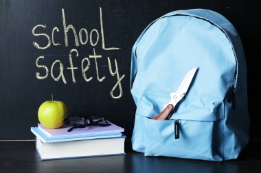 Sırt çantasında bıçak, kitap, defterler, bardaklar ve elma tahtaya yakın siyah tahta masada. Okul güvenliği