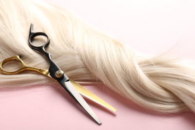 Açık pembe arka planda saç teli ve makas, yakın plan.