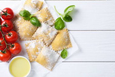 Pişmemiş ravioli, fesleğen, domates ve yağlı beyaz ahşap masa, düz yatak. Metin için boşluk