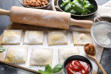 Pişmemiş ravioli, merdane, bolonez, sos ve fesleğen siyah masada, yakın plan.