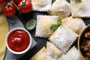 Pişmemiş ravioli, bolonez, sos, domates ve fesleğen siyah masada, düz yatıyordu.