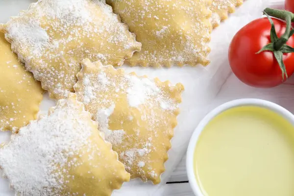 Pişmemiş ravioli, domates ve yağ beyaz ahşap masada, yakın plan.