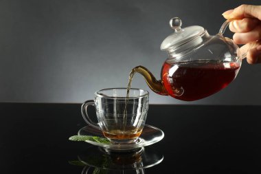 Koyu ayna masasında çaydanlıktan fincana taze demlenmiş çay dolduran kadın, yakın plan.