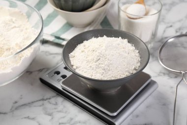 Dijital mutfak terazisi, beyaz mermer masa üzerinde bir kase un ve diğer ürünler, yakın plan.