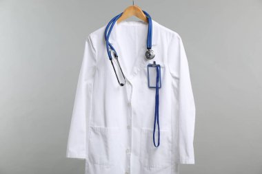 Üzerinde steteskop ve rozet olan doktor ceketi gri arka planda.