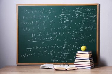 Kitaplar, bardaklar ve elmalar tahtanın yanında, formüllü.