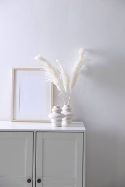 Beyaz duvarın yanındaki dolapta boş resim çerçevesi ve şık ev dekorasyonu