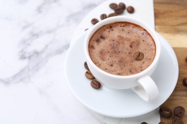 Aromatik kahve fincanda, fasulye ve çay tabağı beyaz mermer masada, yakın plan. Metin için boşluk