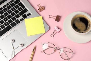 Yapışkan not, kalem, cilt klipleri, bardaklar, kahve, kulaklıklar ve pembe arka planda dizüstü bilgisayarlar.