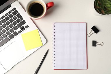 Not defteri, yapışkan not, kalem, cilt tokaları, çiçek dekoru, kahve ve dizüstü bilgisayar beyaz masada, düz yerde.