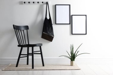 Beyaz duvarda boş resim çerçeveleri, sicim torbası, sandalye ve ev bitkisi