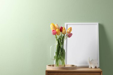 Boş çerçeve, dekor ve güzel laleler komodinin yanında soluk yeşil duvarın içinde, metin için boşluk