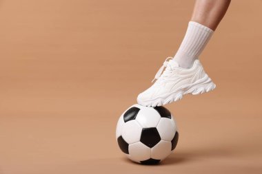 Bej arka planda futbol topu olan spor ayakkabılı kadın, yakın plan. Metin için boşluk