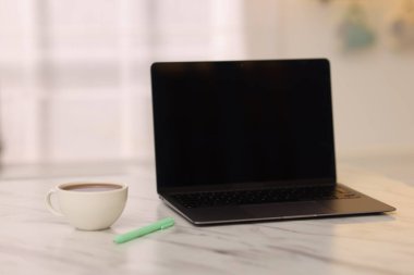 Boş ekranlı dizüstü bilgisayar, bir fincan sıcak içecek ve mutfaktaki beyaz mermer masaya kalem. Tasarım için model