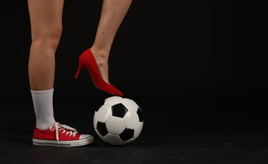 Arka planda futbol topu olan yüksek topuklu ayakkabılı ve spor ayakkabılı bir kadın, yakın plan. Metin için boşluk