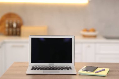 Boş ekranlı dizüstü bilgisayar, akıllı telefon ve mutfaktaki ahşap masada kırtasiye malzemesi. Tasarım için model