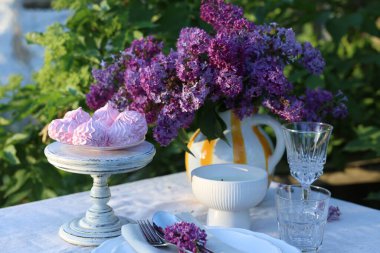 Güzel leylak çiçekleri, zephyrler, tabaklar, çatal bıçaklar, bardaklar ve mumlar bahçede.