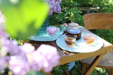 Bahçedeki ahşap masada güzel leylak çiçekleri, tatlılar ve çay.