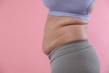 Pembe arka planda göbeği aşırı yağlı bir kadın, yakın plan ve mesaj için yer. Aşırı kilolu