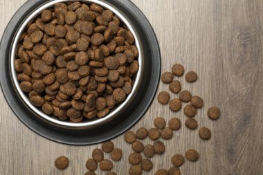 Tahta arka planda besleme kabında kurutulmuş hayvan mamaları, üst manzara.