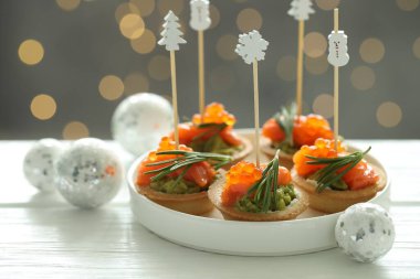 Lezzetli kanepeler ve beyaz ahşap masa üzerindeki Noel dekoru arka planda bulanık ışıklar, yakın plan. Bokeh etkisi