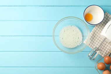 Krem şanti yapıyorum. Kase, el çırpıcı ve malzemeler açık mavi ahşap masada, düz yerde. Metin için boşluk