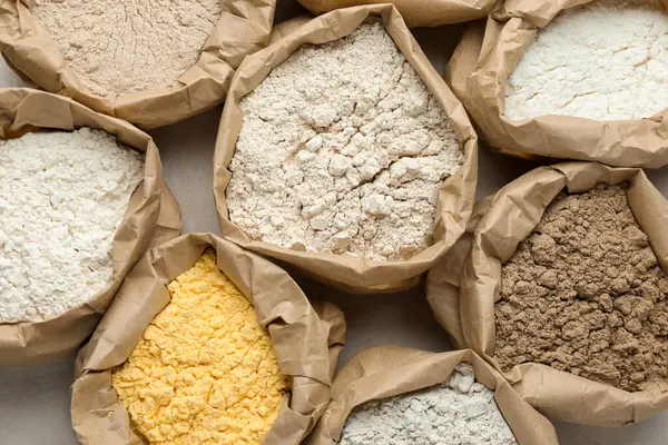 Beyaz masadaki kağıt torbalarda farklı türde un, düz yerde.