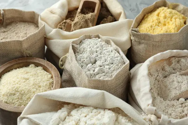 Gri masadaki çantalarda farklı tipte un, yakın plan.