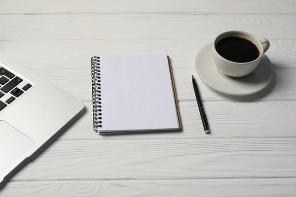 Notebook, pen, coffee and laptop on white wooden table
