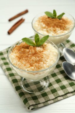 Tarçınlı lezzetli pirinç pudingi ve beyaz ahşap masadaki cam tatlı kaseleri, yakın plan.