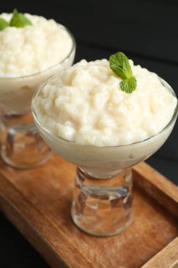 Cam tatlı kaselerinde naneli sütlaç, siyah masada, yakın plan.