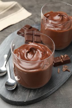 Lezzetli puding ve çikolata parçaları gri masada, yakın plan.