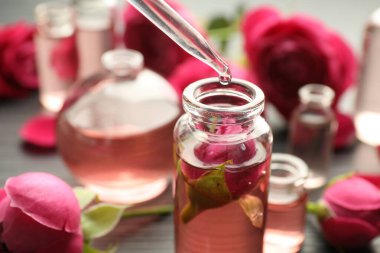 Gri masadaki açık parfüm şişesine yağ damlatıyor, yakın plan.