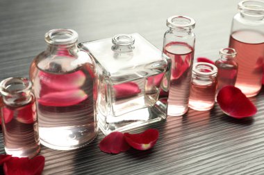 Aromatik esanslı parfüm şişelerini aç. Gri ahşap masada gül yaprakları, yakın plan.