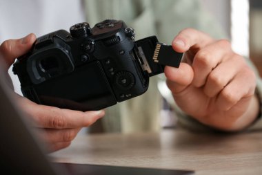 SD bellek kartını içeri, ahşap masadaki fotoğraf makinesine yerleştiren adam.