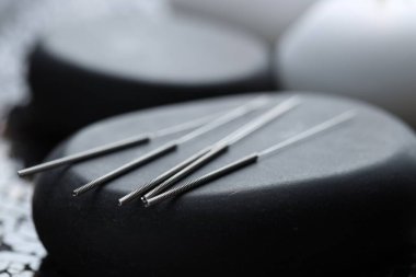 Bulanık arkaplanda akupunktur iğneleri ve spa taşları, yakın plan