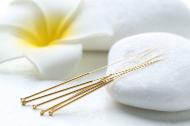 Beyaz arka planda akupunktur iğneleri, spa taşları ve çiçek, yakın plan.