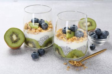 Chia tohumlu lezzetli tatlı, yoğurt, granola, yaban mersini ve kivi açık gri masada, yakın plan. Süper yemek.