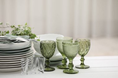 Temiz bardaklar, tabaklar, çatal bıçak takımı ve yeşil saksı.