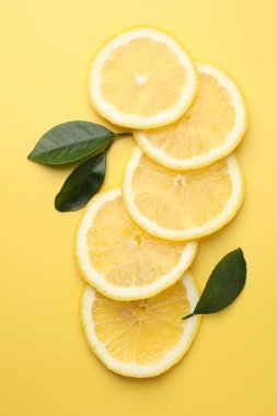 Sarı arka planda taze limon ve yeşil yapraklar var.