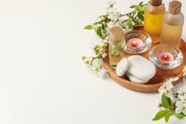 Spa ürünleri, yanan mumlar, çakıl taşları ve beyaz arka planda güzel çiçekli dallar. Metin için boşluk