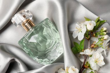 Bir şişe aromatik parfüm ve güzel çiçekli gri ipek kumaş, düz uzanmış