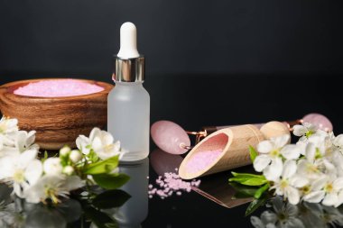 Siyah ayna yüzeyinde kozmetik ürünleri ve güzel çiçeklerle kaplıca kompozisyonu, yakın plan.