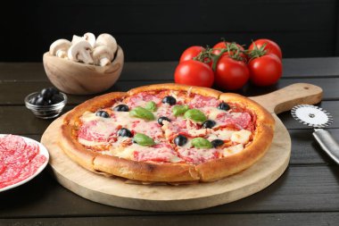 Lezzetli pizza, malzemeler ve siyah ahşap masa, yakın plan.