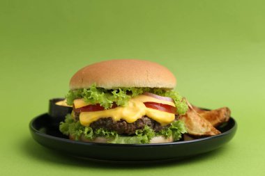 Soslu lezzetli çizburger ve yeşil arka planda patates dilimleri, yakın plan.