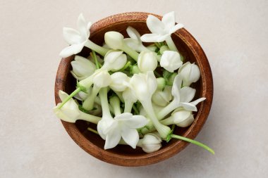 Üzerinde yasemin çiçekleri olan bir kase bej masa, üst manzara.