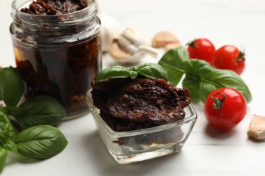 Lezzetli güneşte kurutulmuş domatesler, taze sebzeler, fesleğen ve sarımsak beyaz masada, yakın plan.