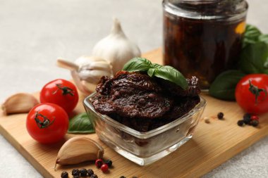 Lezzetli güneşte kurutulmuş domatesler, taze sebzeler, fesleğen ve sarımsak açık gri masada, yakın plan.