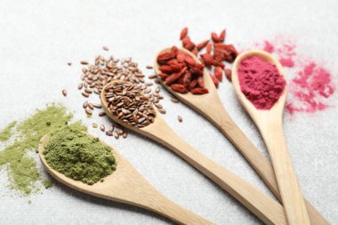 Açık gri masada kaşıklarda farklı süper yiyecek tozları, yakın plan.