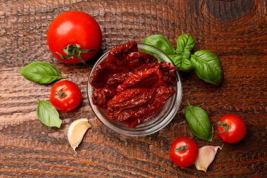 Lezzetli güneş, cam kasede kurutulmuş domatesler, taze sebzeler ve ahşap masada baharatlar, düz uzanmış.